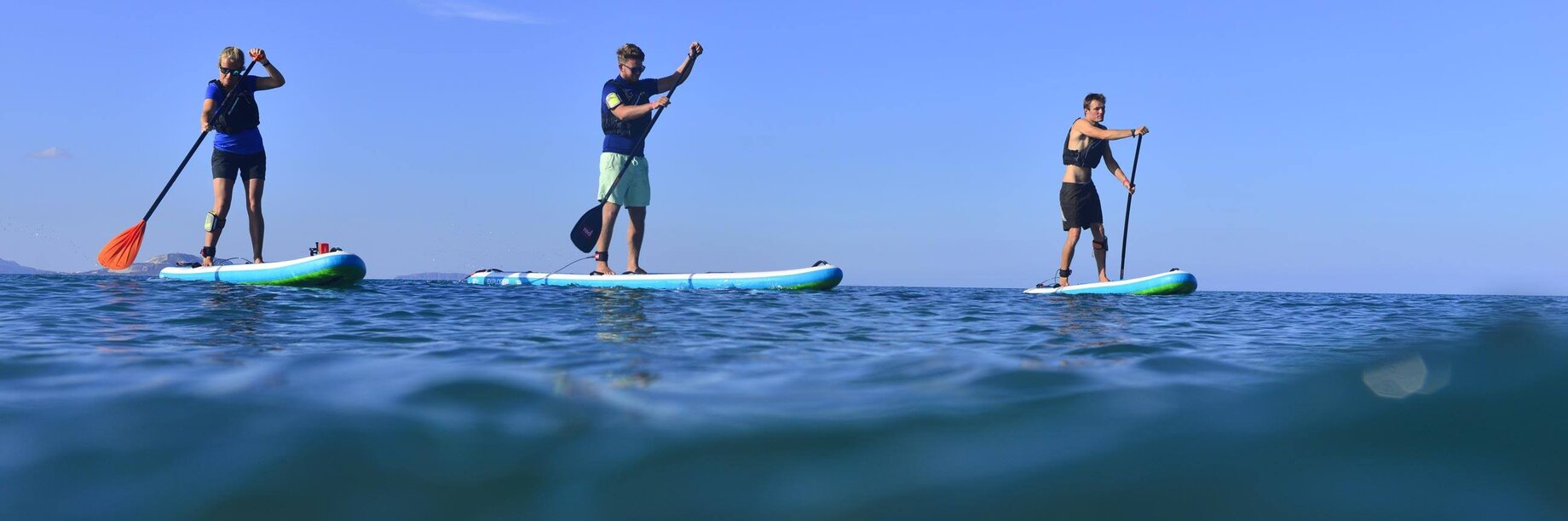 Three people standing up on paddle boards and learning to paddle board on the sea on a Mark Warner holiday