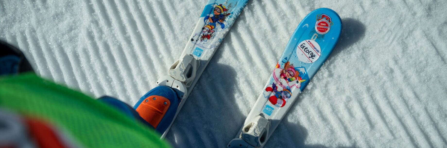 Looking down at the tips of children's skis on fresh corduroy piste