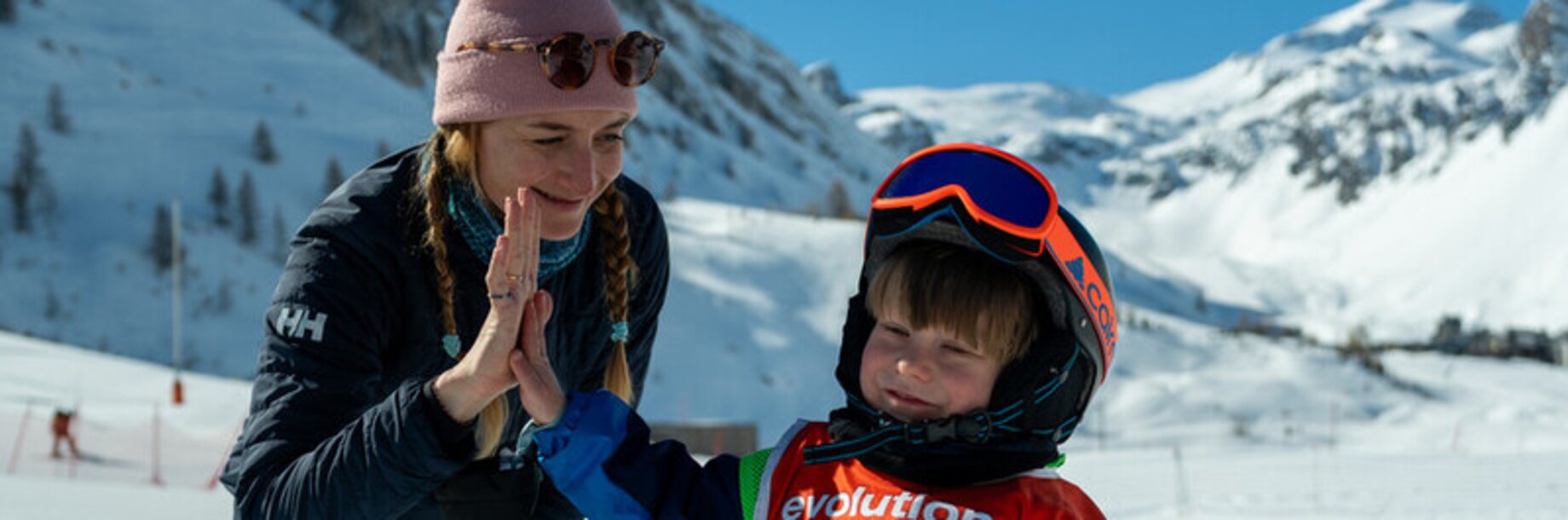 Child high fiving his ski instructor on the piste