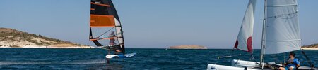 A catamaran sailing alongside a foiling windsurfer