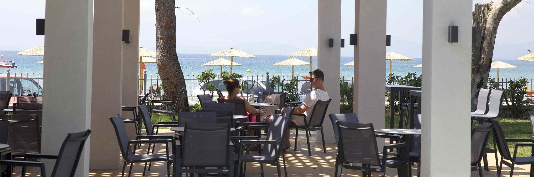 a couple of people sitting at a table in a patio with a body of water in the background