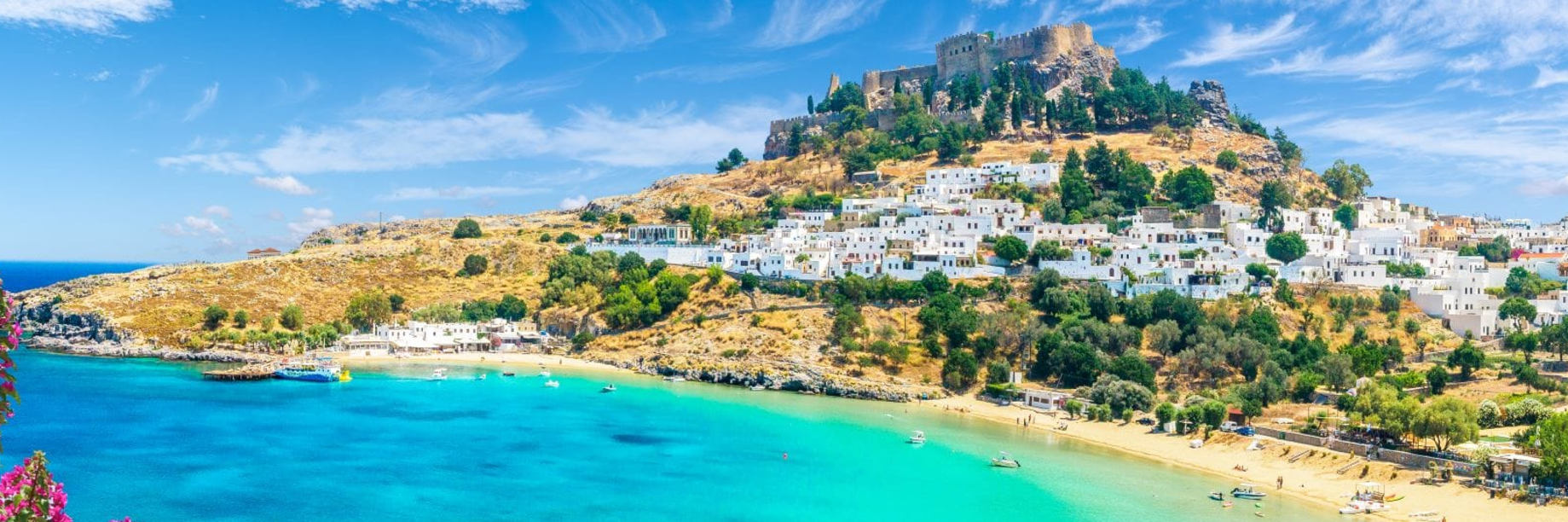 An image of the whitewashed town of Lindos and the Acropolis in St Paul's Bay, Rhodes with turquoise sea and a sandy beach